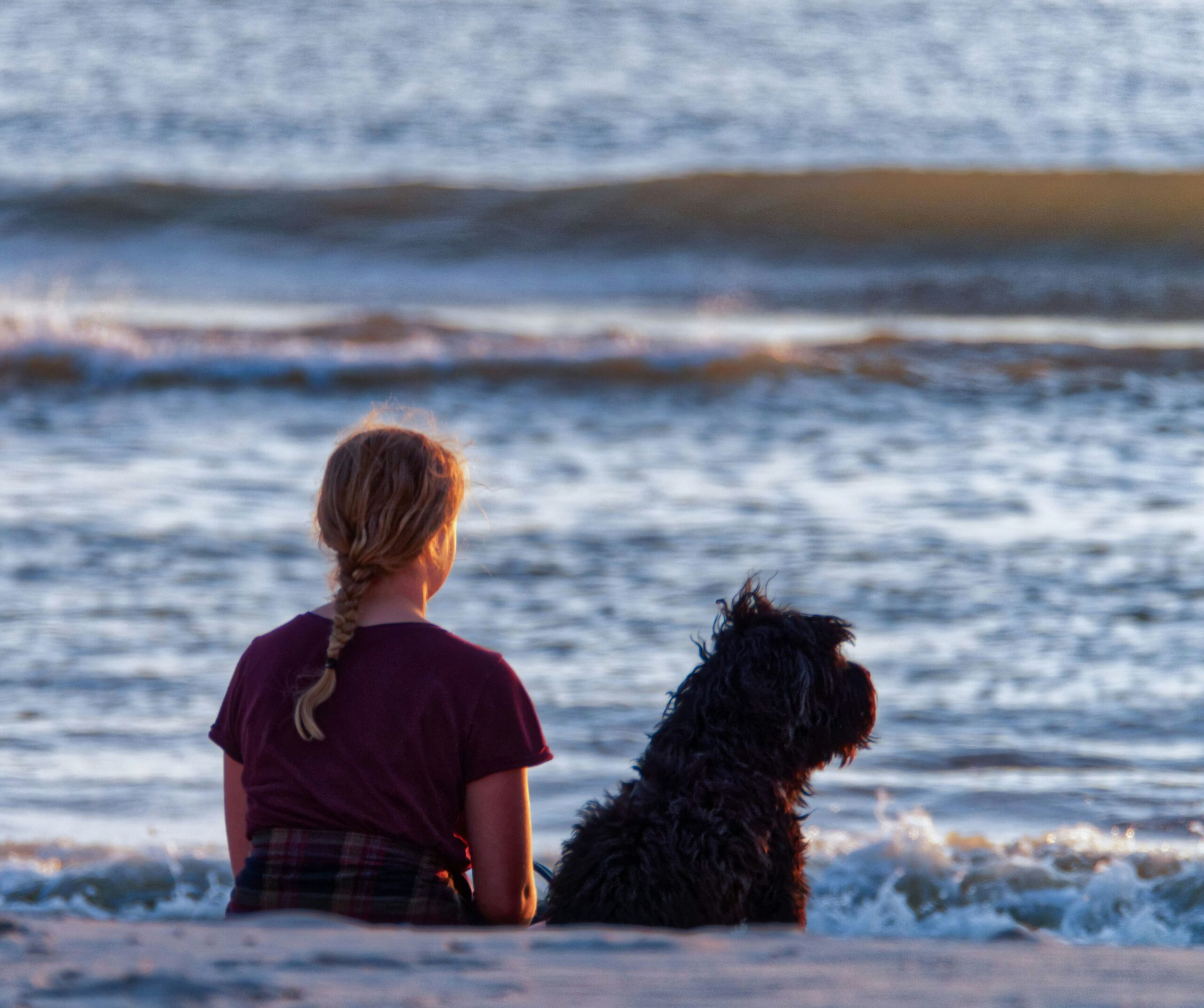 Ein Kind und ein Hund sitzen Seite an Seite am Wasser.